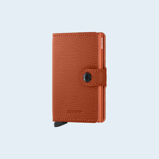 Secrid Miniwallet Crisple Pumpkin tegen een zachte pastelachtergrond (lichtblauw)