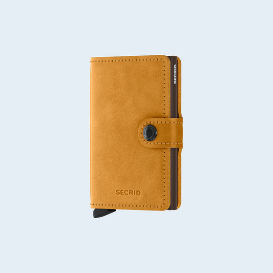 Secrid Miniwallet Vintage Ochre tegen een zachte pastelachtergrond (lichtblauw)
