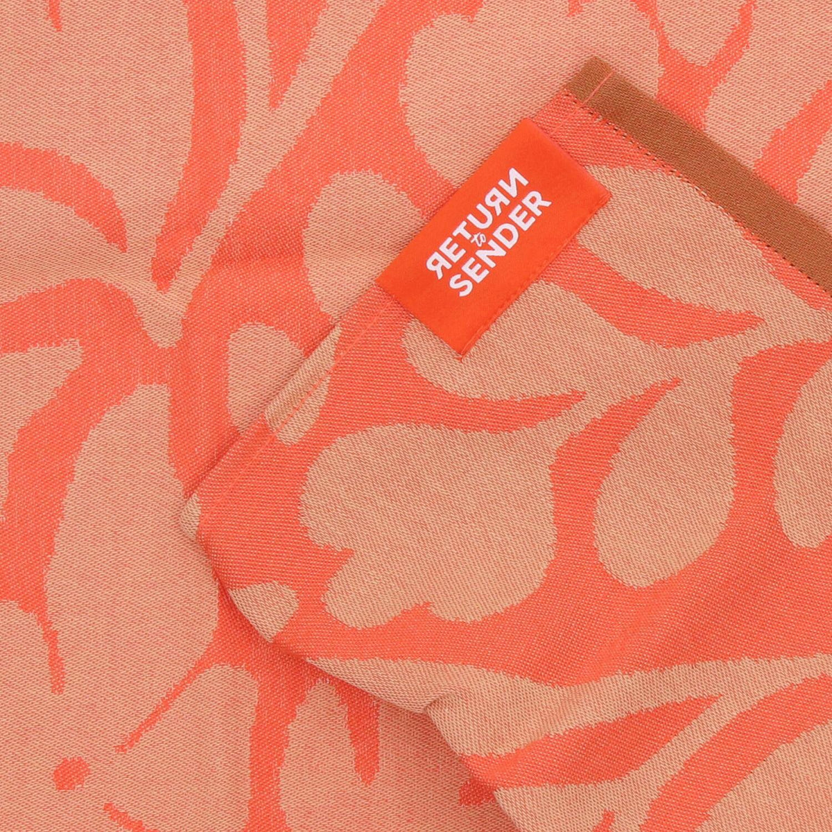 Detail van het koraalkleurige Carina bloemendessin en Return to Sender-label